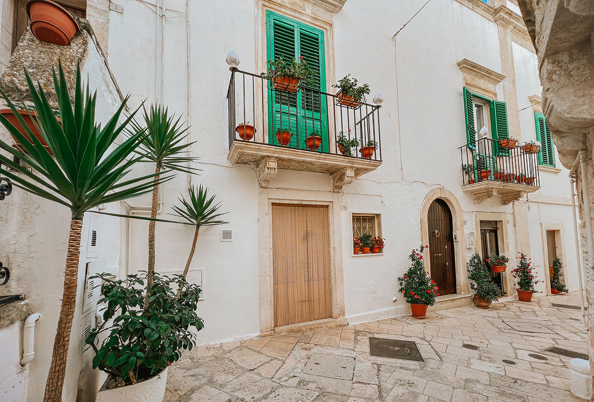 Traditional whitewashed houses with green shutters along a quiet street in Locorotondo, Puglia