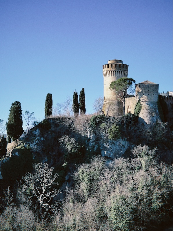 Hilltop view of Brisighella’s Rocca dei Veneziani framed by olive trees and countryside.