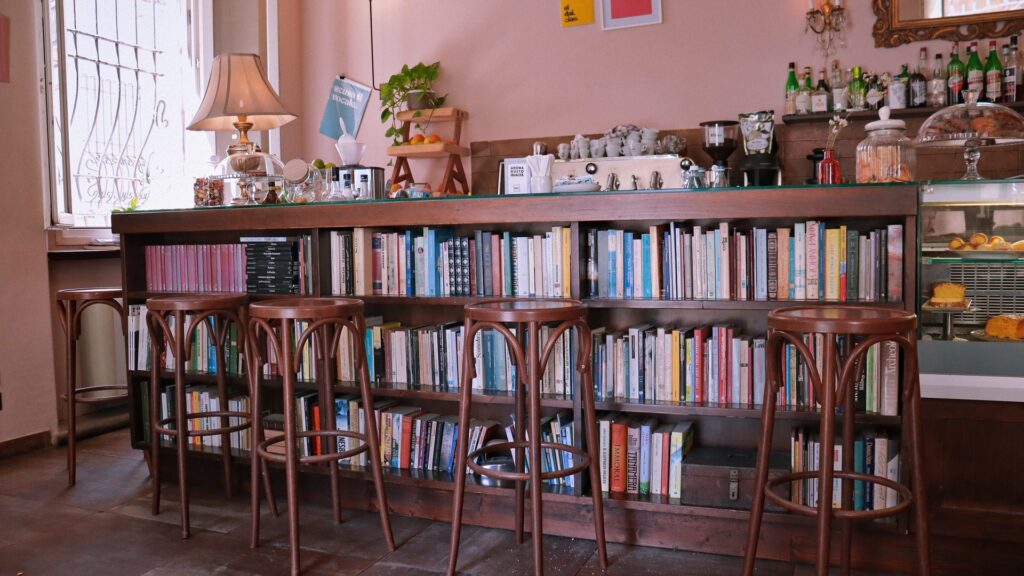 Book-lined cafe bar with wooden stools, pastries, coffee station, and pink walls in a welcoming Italian interior