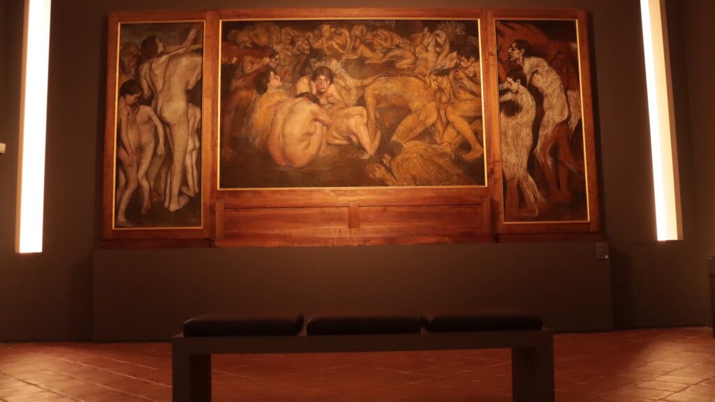 Dramatic triptych painting displayed in Faenza Pinacoteca with warm lighting and a simple black bench
