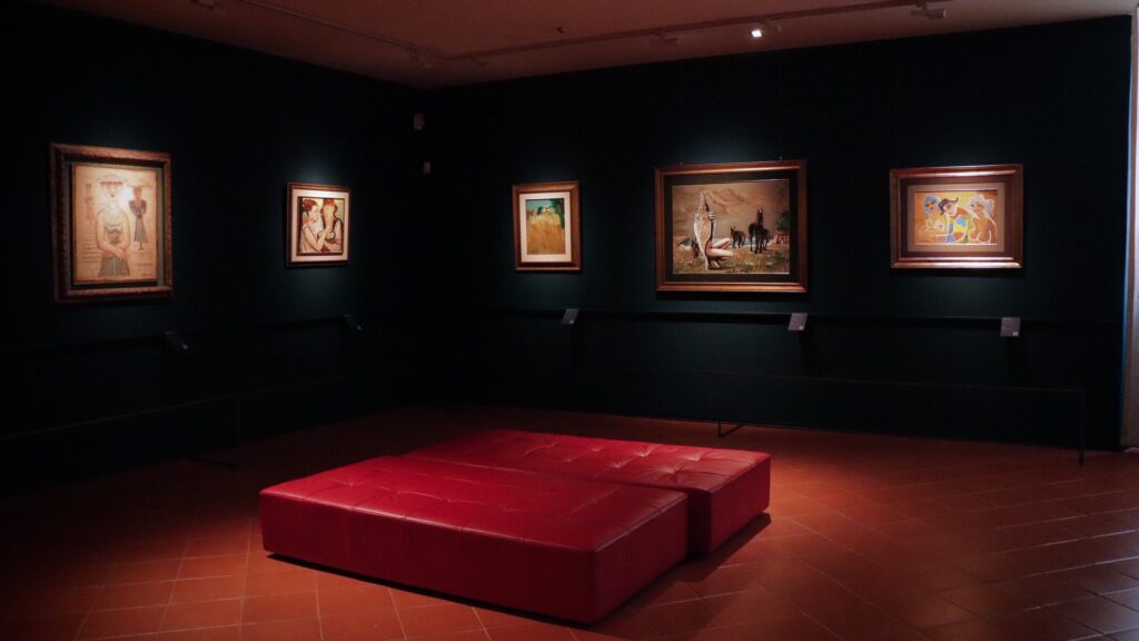 Dark Faenza Pinacoteca museum room with framed artworks on green walls and red seating under spotlights