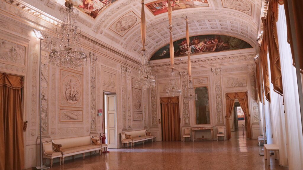 Grand Palazzo Milzetti hall with chandeliers, frescoed ceiling, carved walls, and polished marble floor