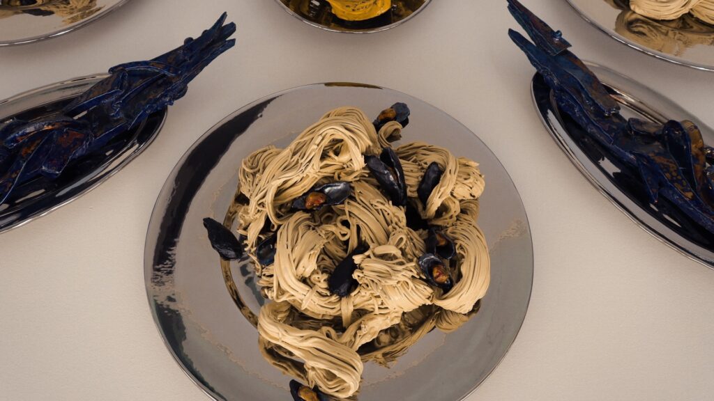 Ceramic pasta and mussel artwork arranged on plates, blending Italian food culture and contemporary ceramics