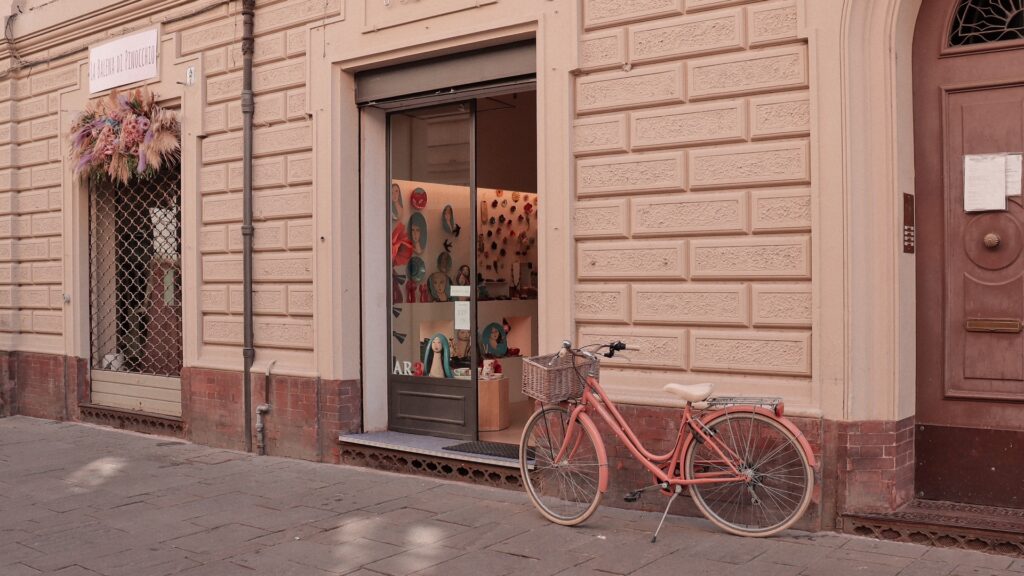 Pink bicycle parked outside an artisan storefront on a quiet Faenza street