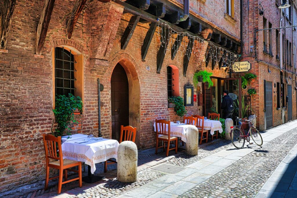 Outdoor trattoria tables on a cobblestone street for planning an Emilia-Romagna travel budget